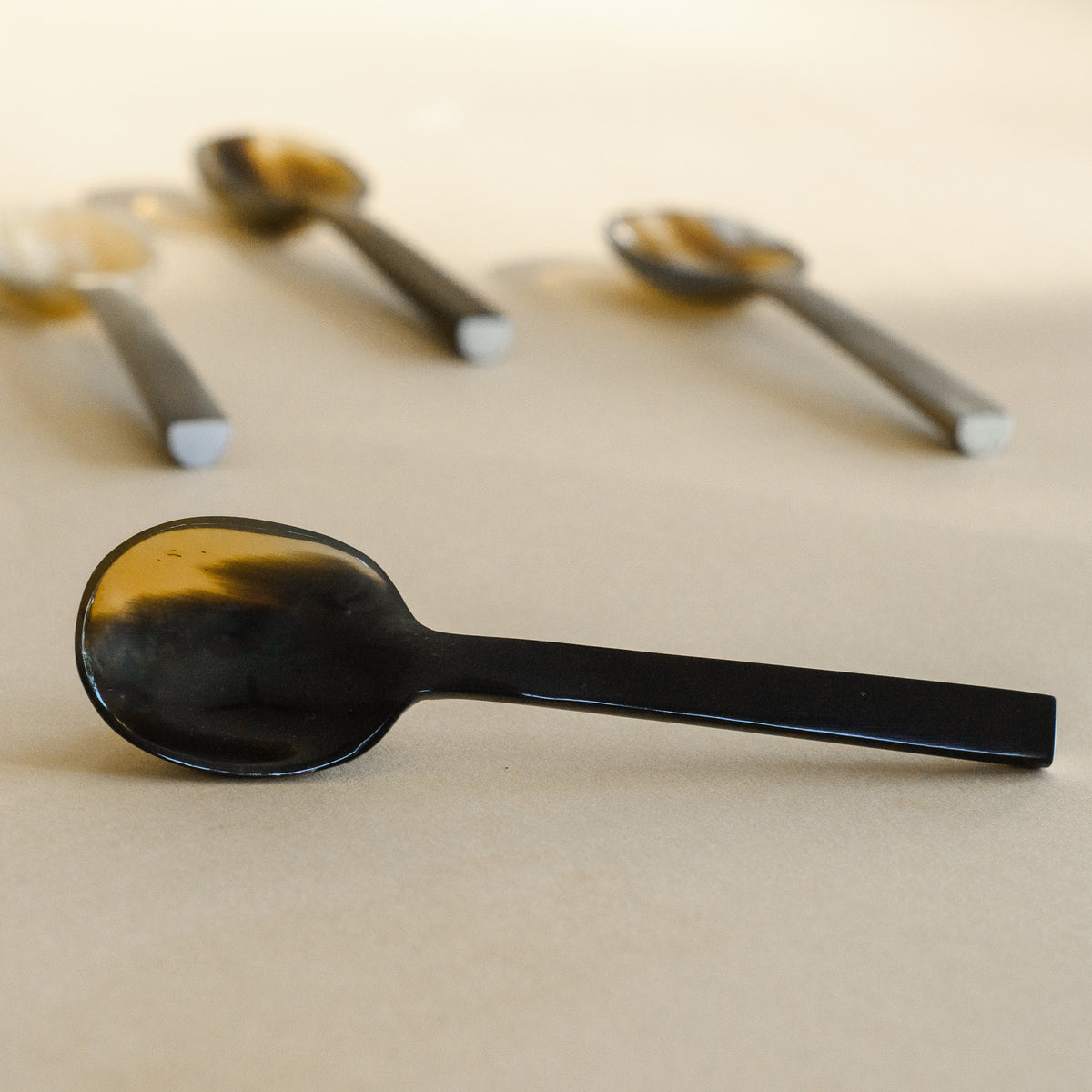 A closeup of a small horned marble coffee spoon, with three additional spoons in the background.