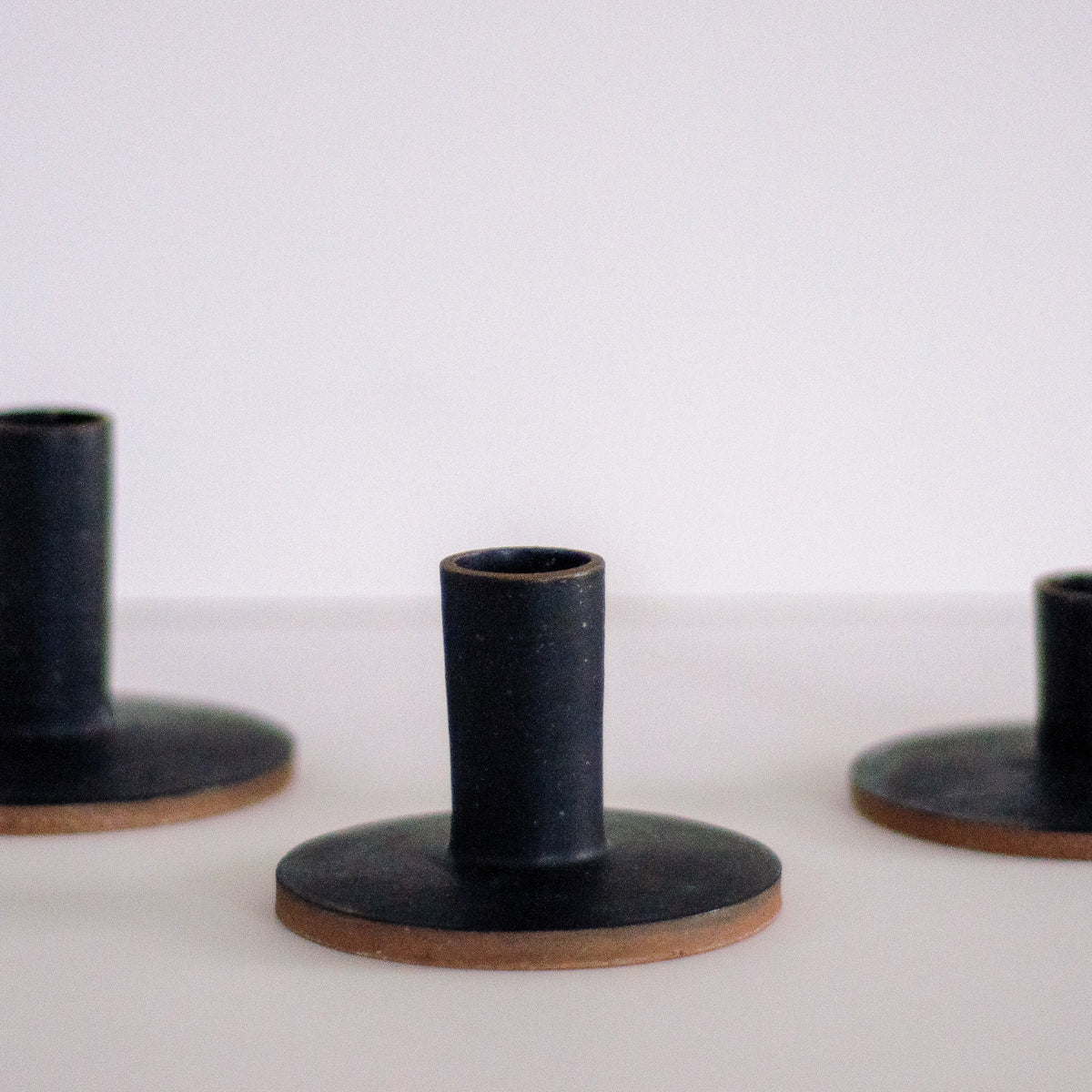 three black taper candle holders on a neutral surface, with one in focus and the others out of focus.